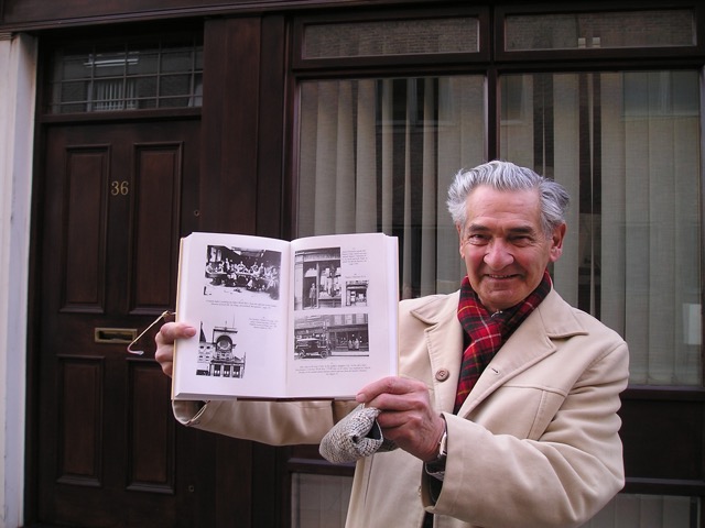 Cyril showing picture in book &ldquo;My Family&rdquo; (written in 1996) of house where he was born.